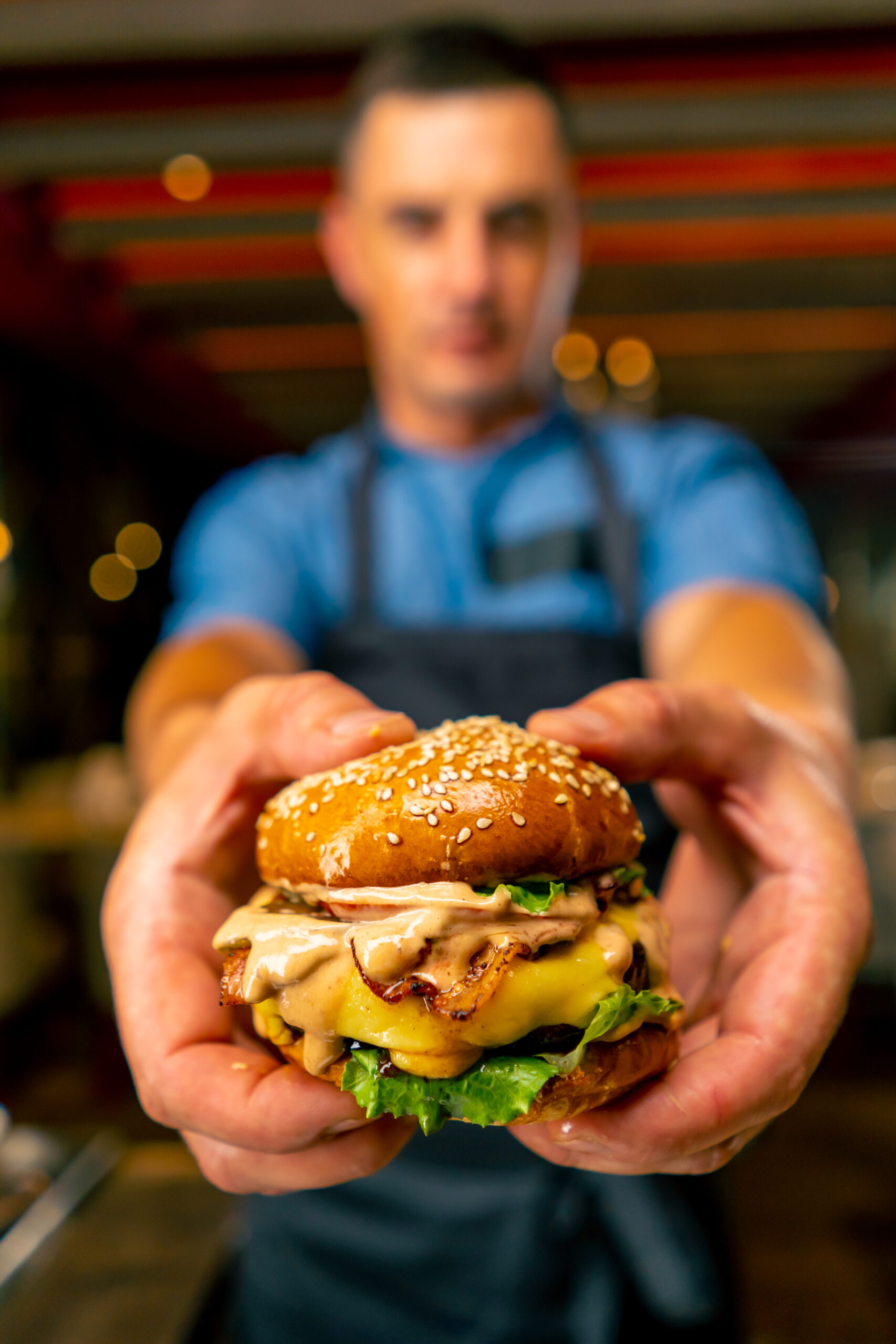 The chef of an italian restaurant in uniform shows the burger he cooked in his professional kitchen